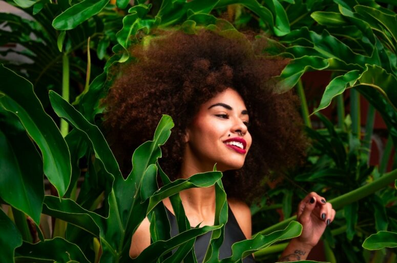 A lady with brown curly surrounded with green leaves